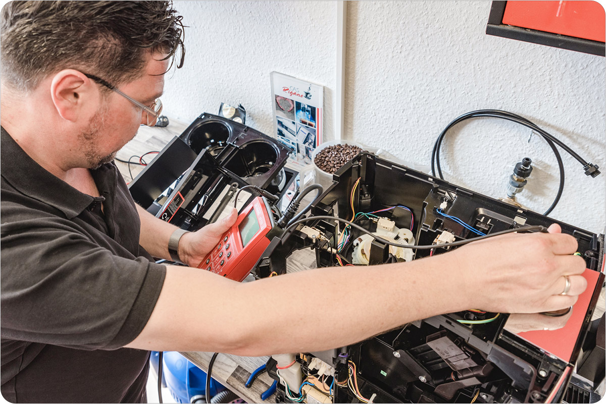 Deko: Techniker mit Messgerät an offenem Kaffeeautomaten, von schräg oben